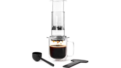 AeroPress Clear coffee press brewing into a glass mug, with scoop and stirrer