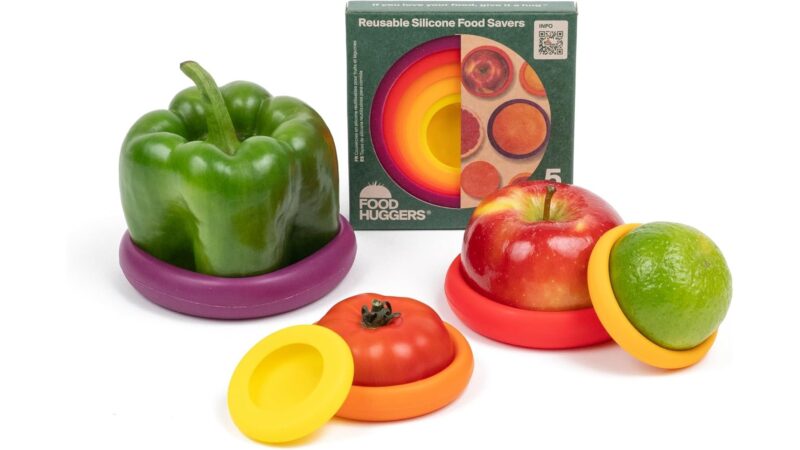 Food Huggers silicone food savers capping a pepper, tomato, apple and lime next to the box