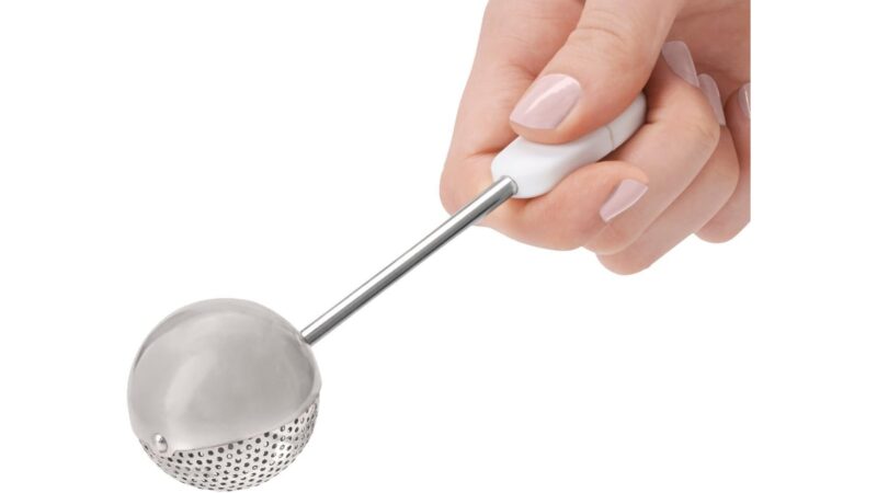 Hand holding an OXO Good Grips baker's dusting wand with a stainless steel mesh ball
